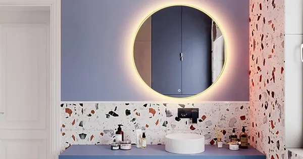 Round mirror with warm light above a washbasin and a terrazzo wall